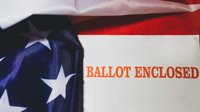 Red text “Ballot Enclosed” with portions of an American flag in the background.