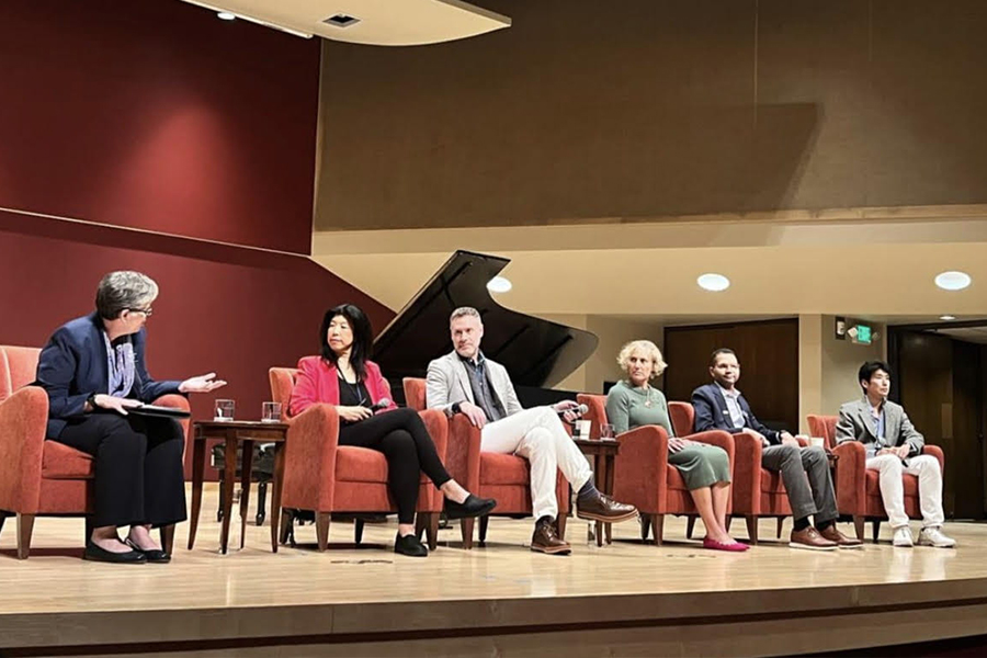 President Sarah Bolton moderating a panel of five alumni, seated in chairs on a stage.