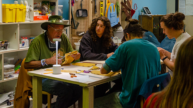 Roger Amerman and three students sit at a crafting table.