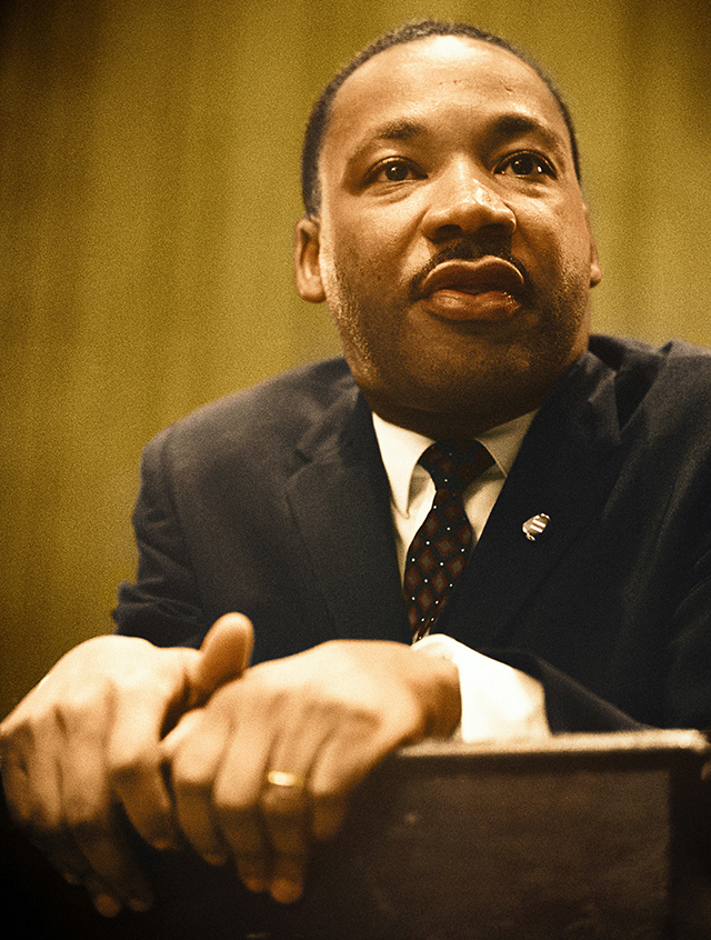 Martin Luther King Jr., wearing a suit, with hands on a podium.