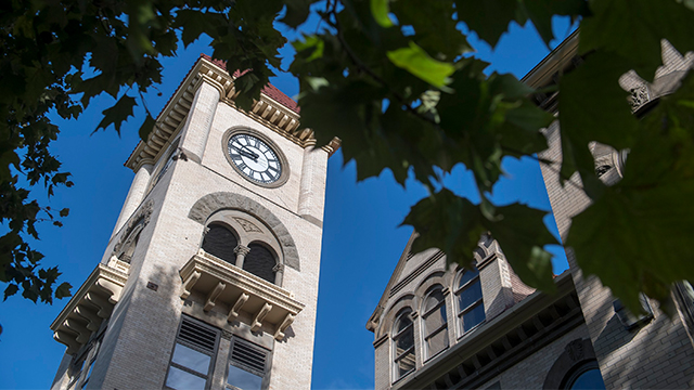 The clock tower of Memorial Building framed by nearby tree branches and leaves.