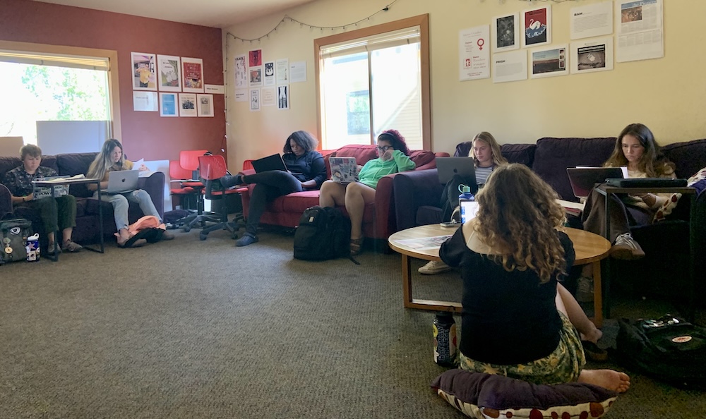 A group of students in Introduction to Social Justice class sit on chairs and couches in the Glover Alston Center working on laptops.