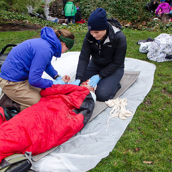 Whitman Students helping someone laid out on the ground in the practicing first responders aid .