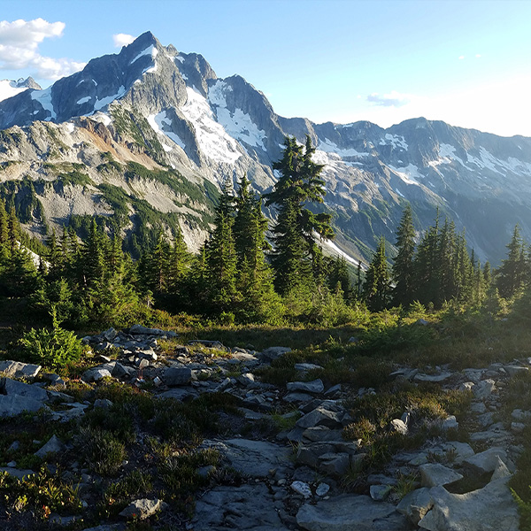 A landscape showcasing a green mountain with some snow towards the top of the mountain.