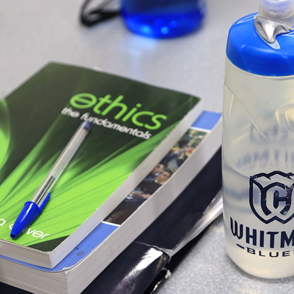 A Whitman College water bottle next to an ethics textbook.