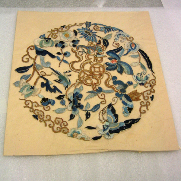 Circular embroidery glued on paper with a flower and bird design.