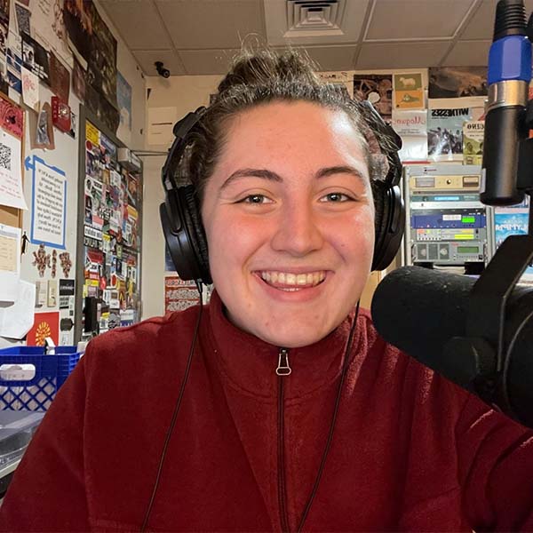 A Whitman student sitting in the student radio station booth with a microphone in front of her.