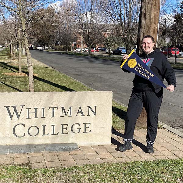 Zoe Perkins, holding a pick-axe, standing next to a Whitman College sign. 