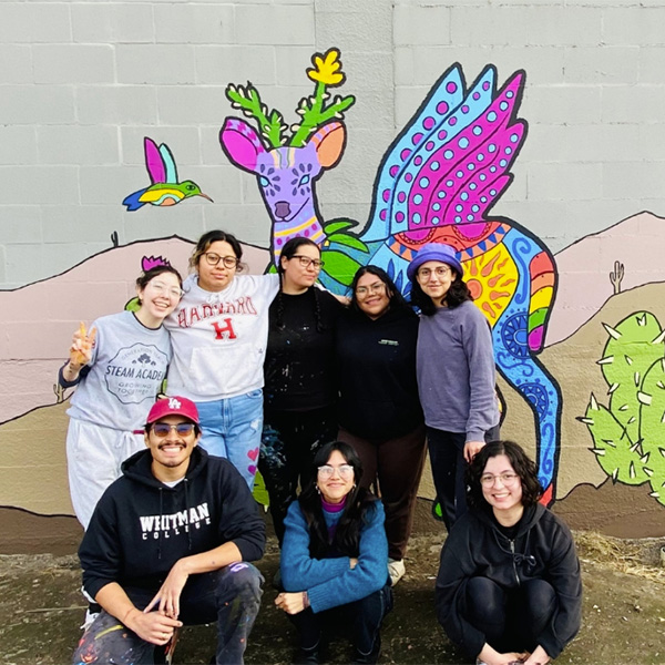 Whitman College students a part of Unidos standing in front of a mural.