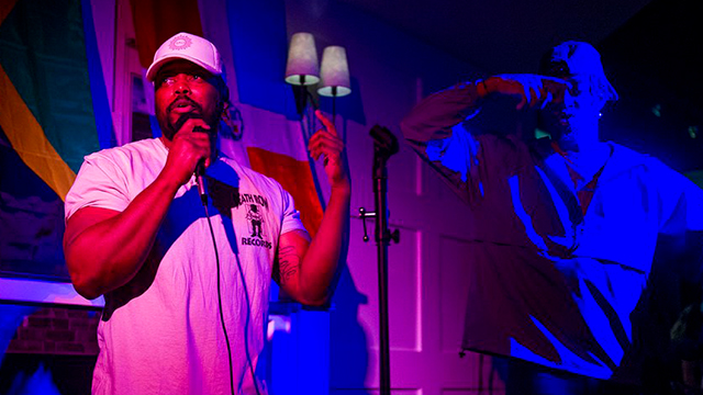 On the left, a hip-hop performer with microphone under pink and red lights; on the right, the silhouette of another performer under blue light.