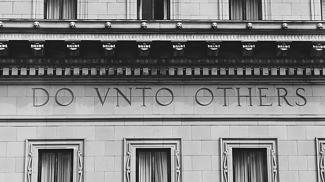 Black and white image of the side of a building with the words "DO VNTO OTHERS"