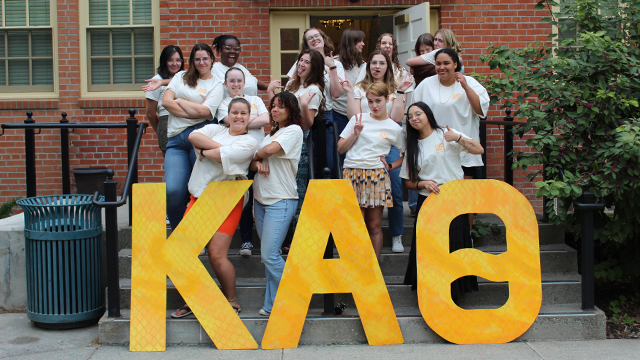 A group of sorority members make silly poses with three giant Greek letters.