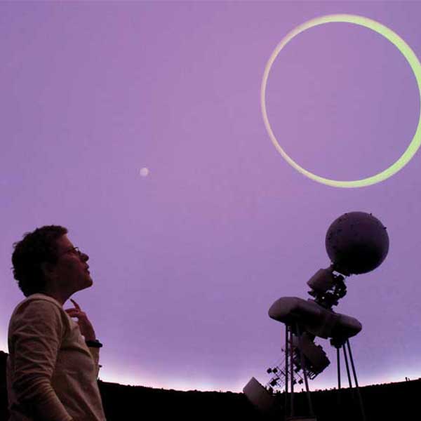 Andrea Dobson looking up at a circle of light emitted from a telescope.