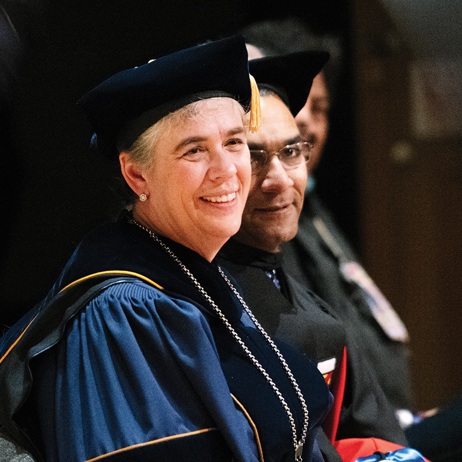 President Sarah Bolton in cap and gown sitting with peers.