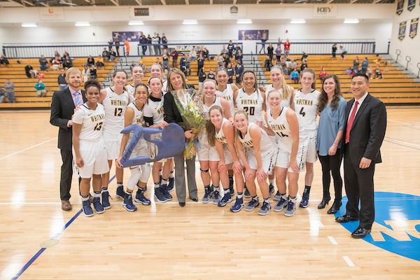 The women's basketball team celebrates their 250th win, against Pacific Lutheran University in January 2017, with Head Coach Michelle Ferenz (holding flowers). 
