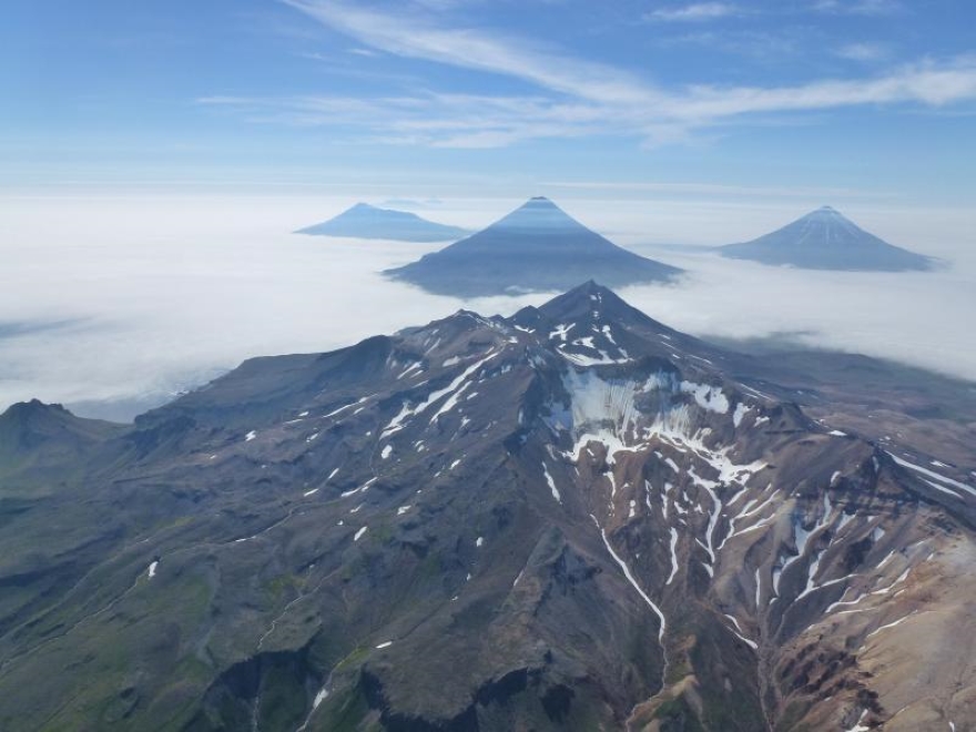 An aerial photo of the volcanoes in the Islands of Four Mountains, Alaska. The summit of Mount Tana is visible in the center. Behind Tana are (left to right) Herbert, Cleveland and Carlisle volcanoes. Photographed by John Lyons of the USGS. 