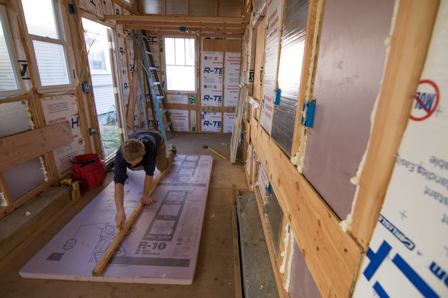 Kneeling on the floor of the tiny house, Preskenis measures a board for placement inside the tiny house