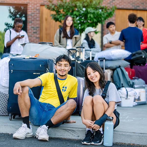 Two Whitman College students sitting on the curb with move inbelongings in the background.