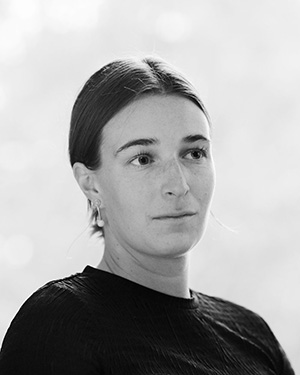 Black and white portrait of Georgia Cloepfil. Her hair is parted in the middle and pulled back and she is wearing a dark colored sweater and looking off to the side.