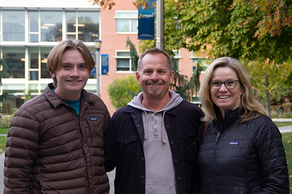 Two parents and their child posed in front of the science building.