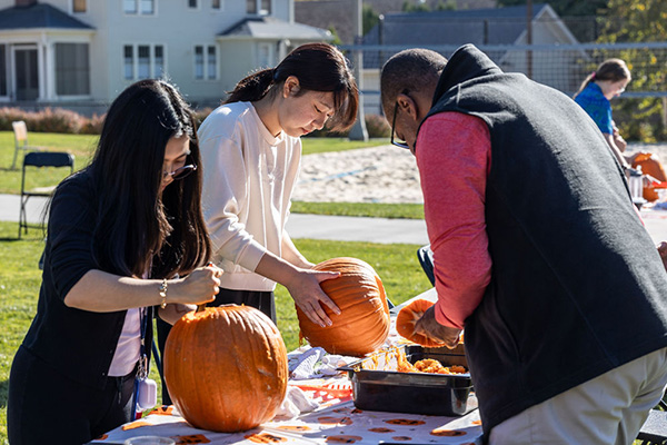 Three people carving pumpkins on a picnic table outdoors.