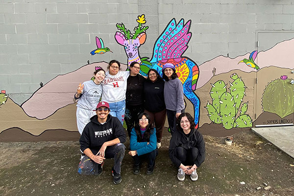 Whitman College students standing in front of a colorful mural.