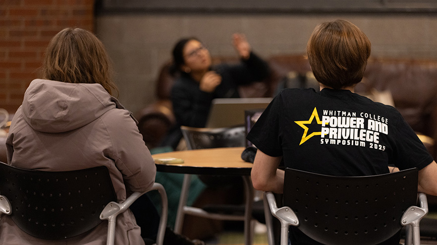 Several seated students. One wears a black T-shirt with the text "Whitman College Power and Privilege Symposium 2025" 