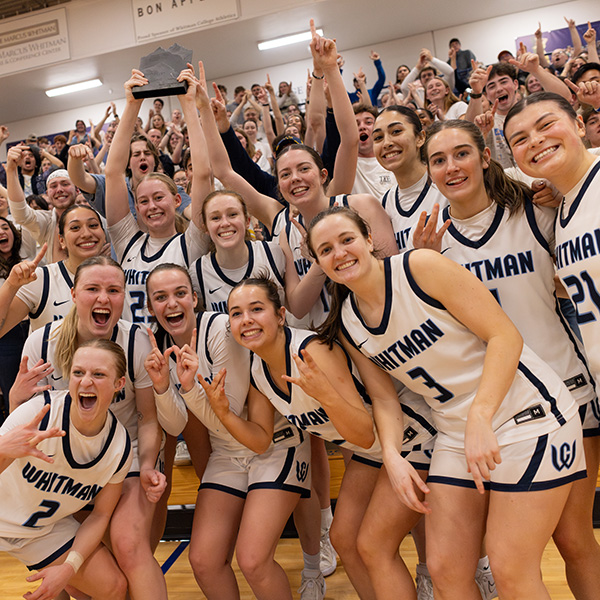 Whitman's women's basketball team poses with trophy in front of a cheering crowd