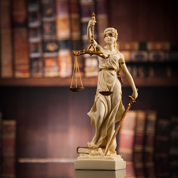 Image of lady justice in front of a book case.