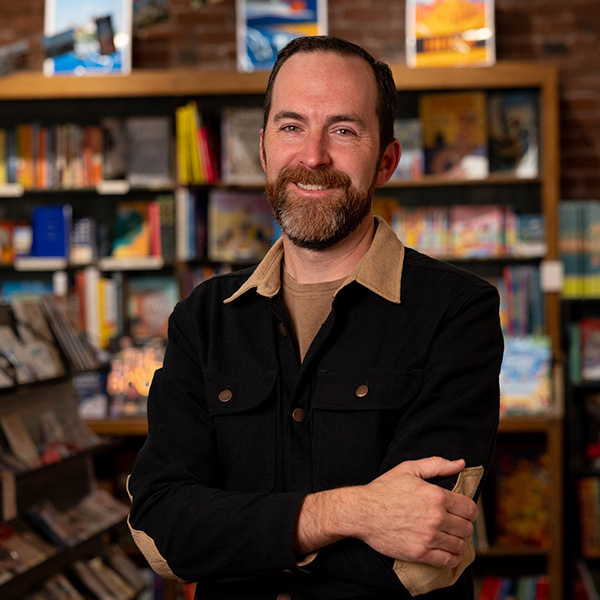 Patrick Leonard posing in front of shelves of books.