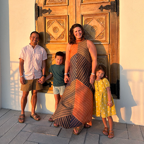 Two adults and two children standing outside in front of a carved wooden door.