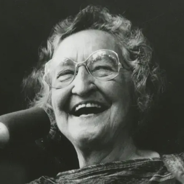 Black-and-white closeup of a smiling Faith Petric in front of a microphone 