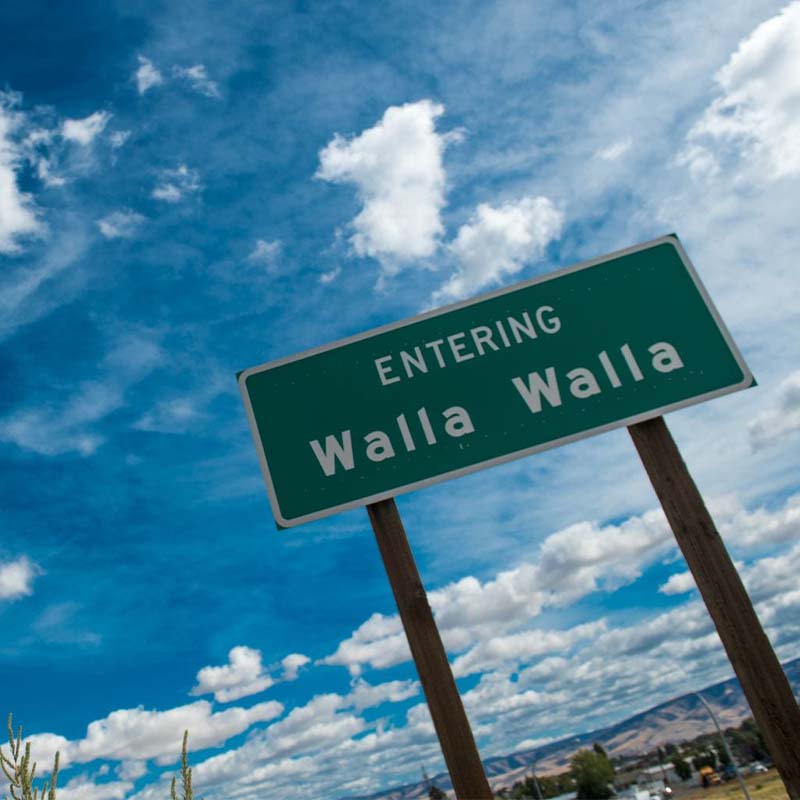 Walla Walla welcome road sign with sunshine and clouds behind it.