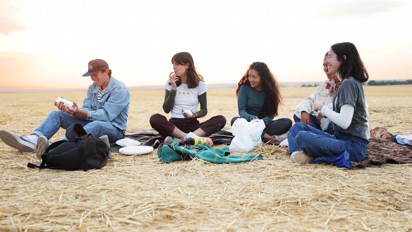 Whitman College students sitting in a wheat field eating burritos.